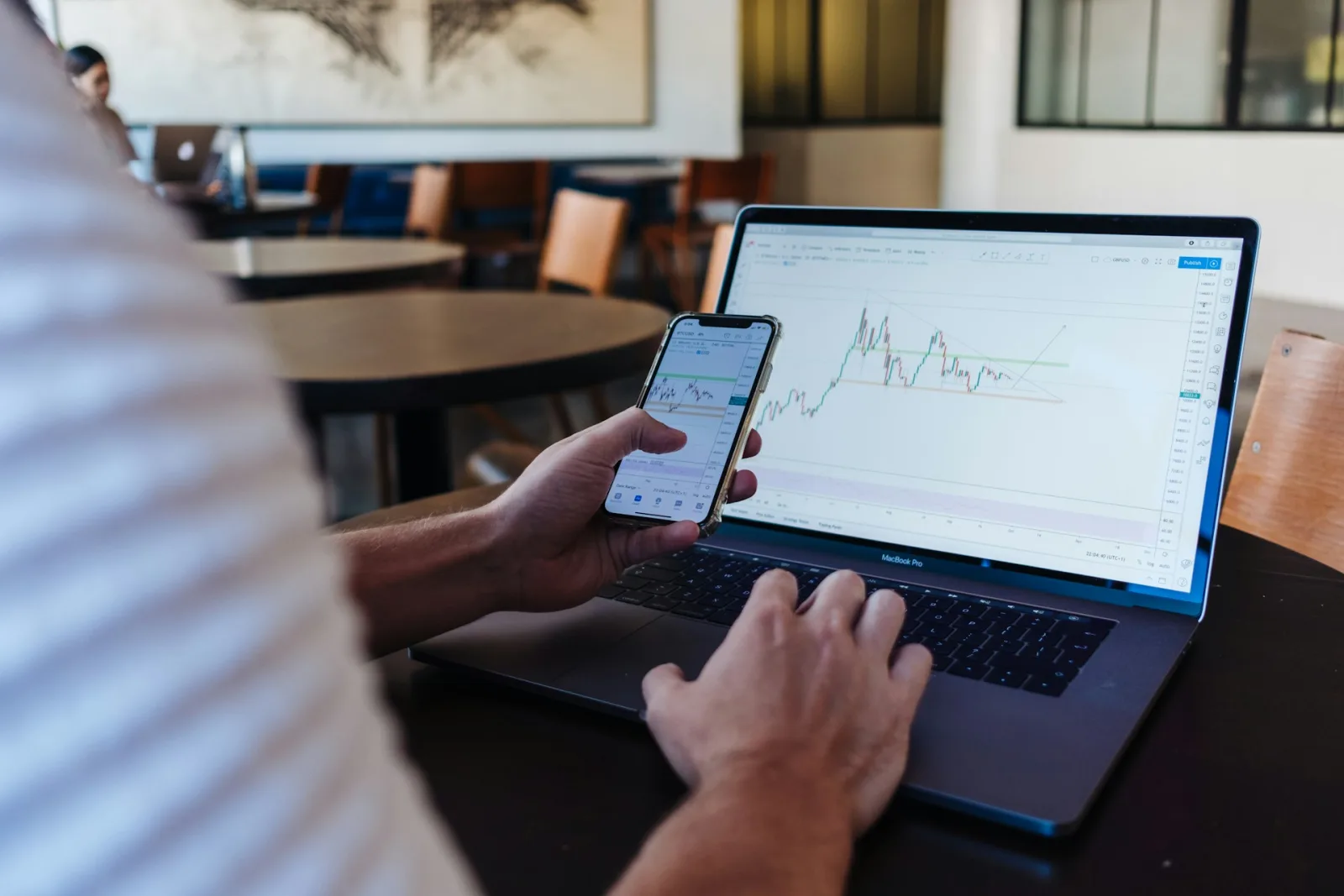 žmogus naudojantis išmanųjį telefoną ir macbook pro